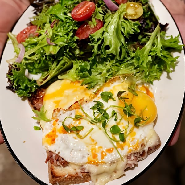 A Croque Madame with a fried egg and melted cheese, served with a fresh green salad.