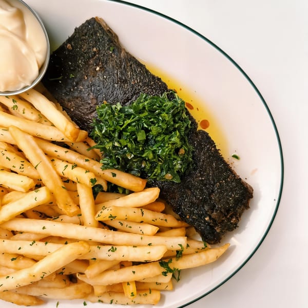 A French dish of dark fish with green herbs, golden fries, and a side of creamy sauce.