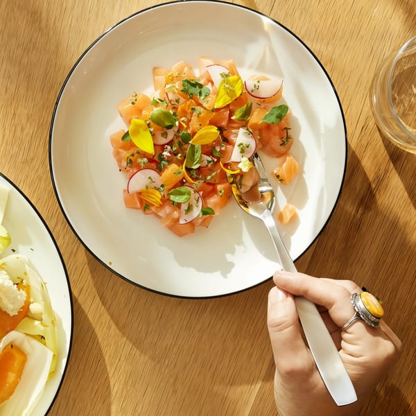 Overhead view of a hand with a ring holding a fork, poised over a salmon tartare dish.