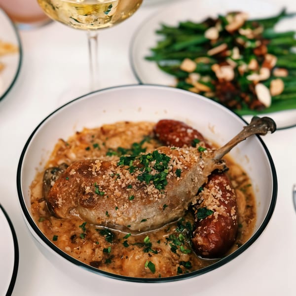 French duck confit with sausage, beans, and a glass of white wine.